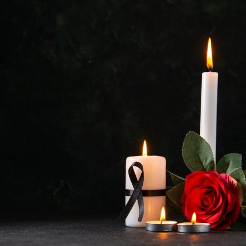 front view of burning candles with red flower on dark background evil funeral death